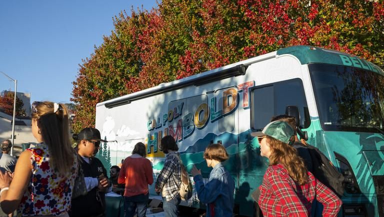 Folks standing in front of the Mobile Alumni Center with trees in the background.