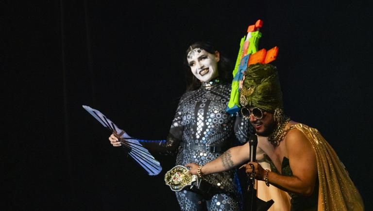Two drag queens in costume with a black background.