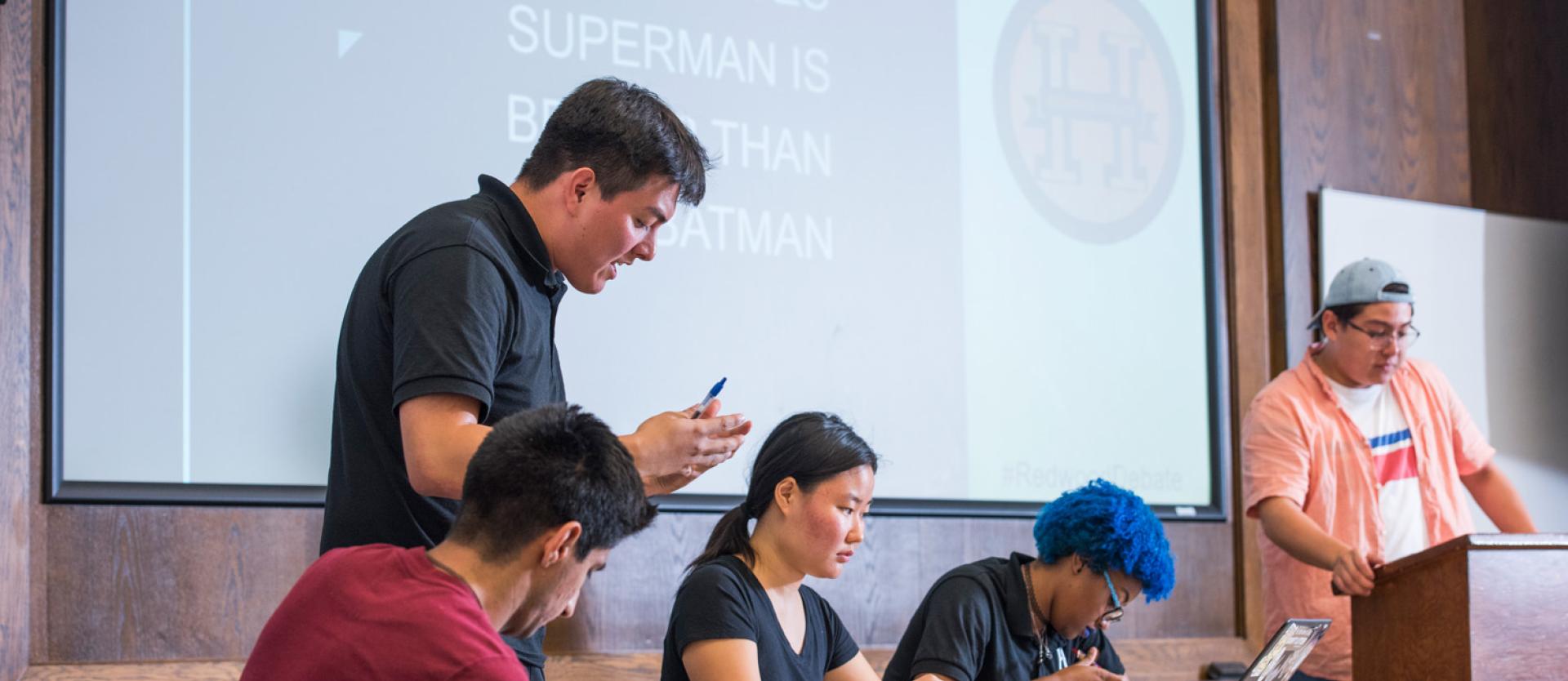 students at a table with a presentation behind them