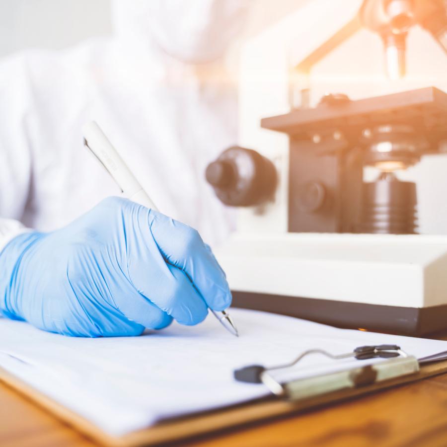 scientist writing notes, microscope in background scientist writing notes, microscope in background