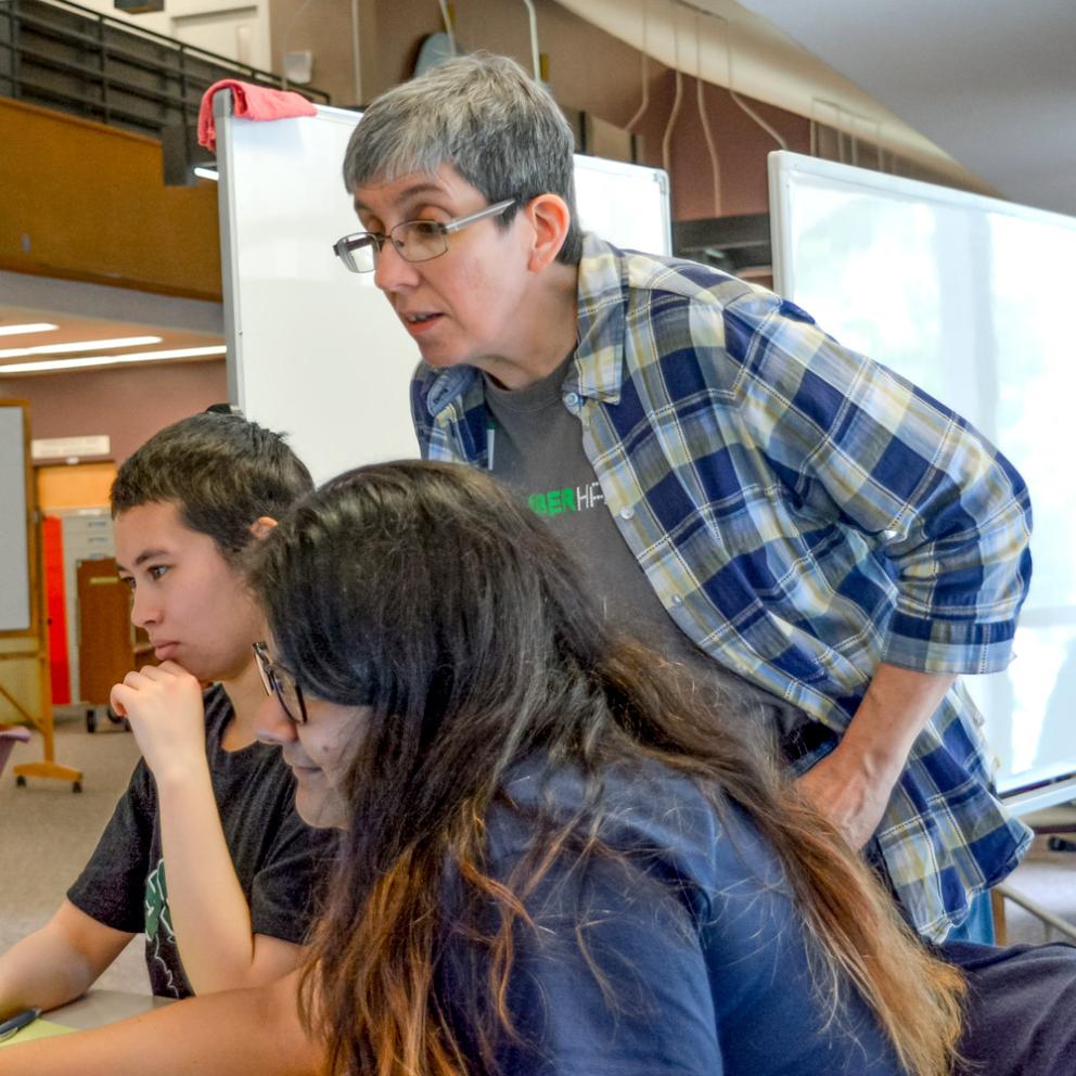 Teacher standing over two students in the library