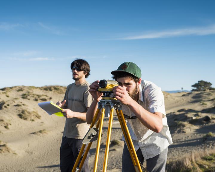 Two people on the beach using surveying equipment