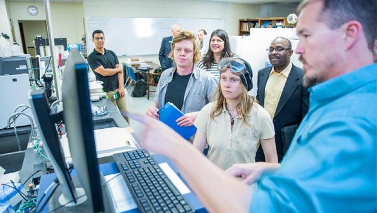 Professor in front of a computer with students in the lab