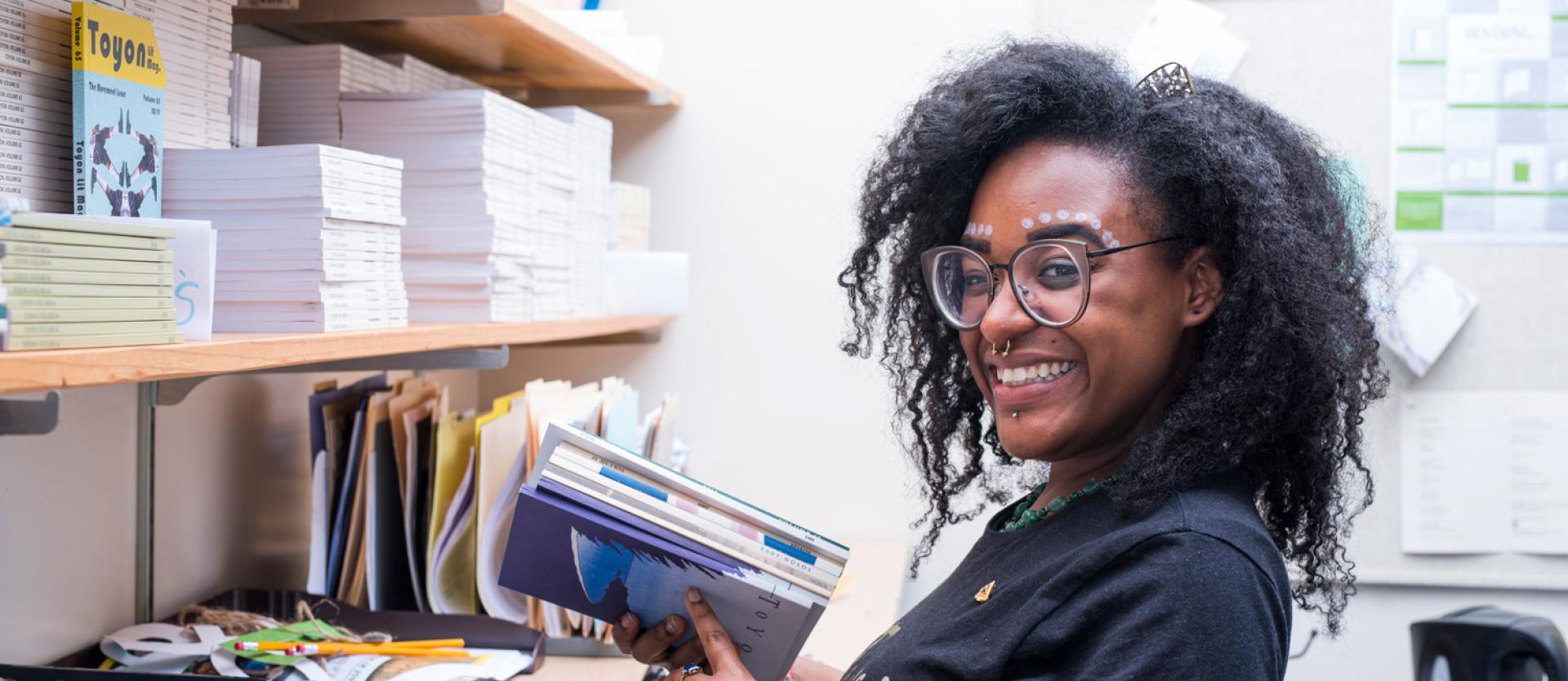 Students with glasses and a small amount of face paint holding a book and smiling at the camera