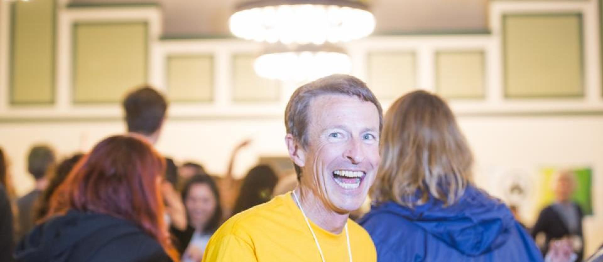 Paul smiling for the camera wearing a yellow shirt