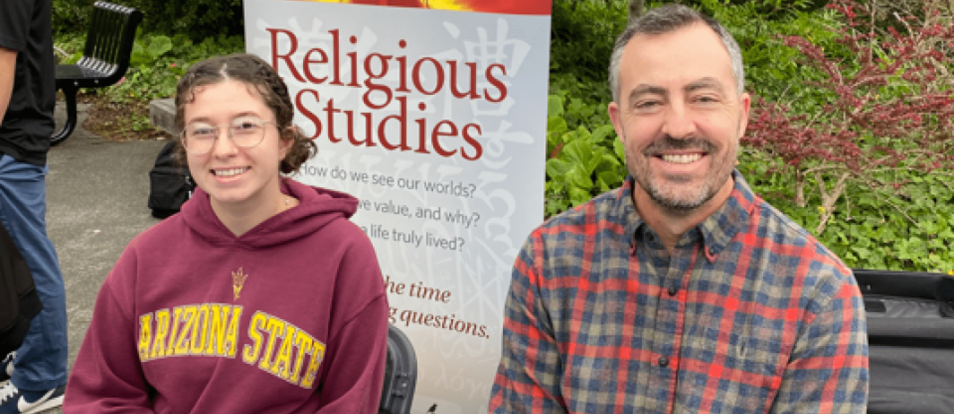 Student and professor sitting in front of a religious studies poster