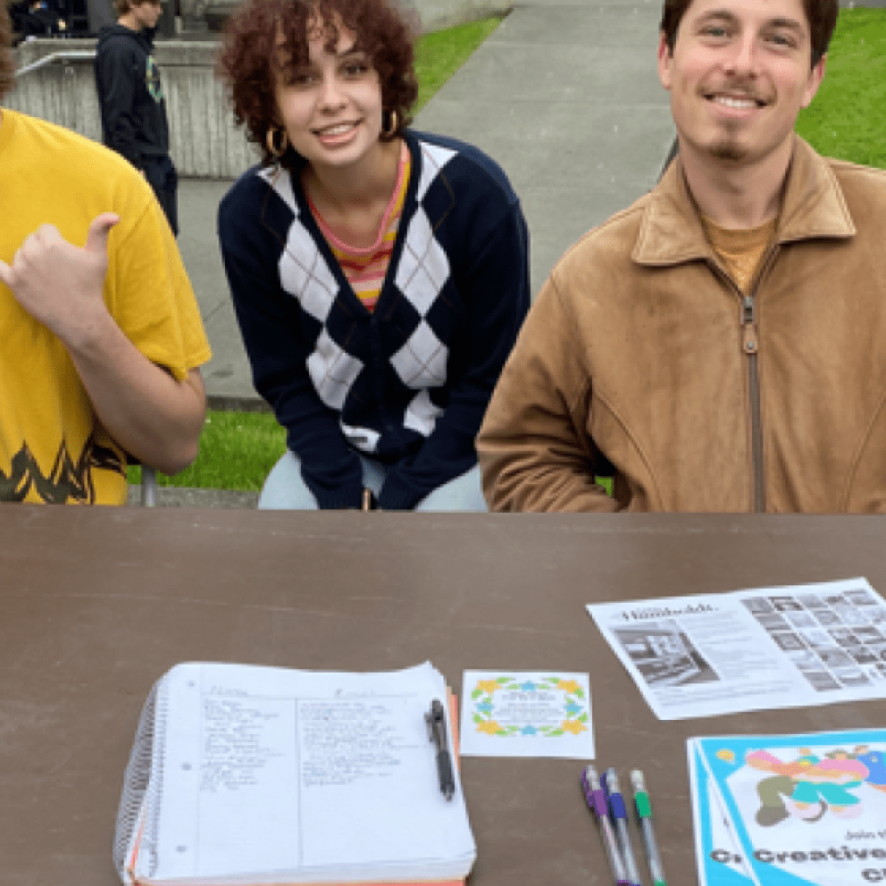 three students at a brown table with papers on it