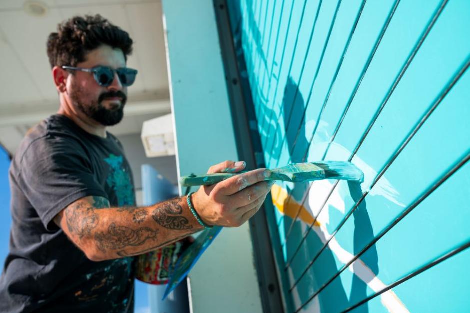 A photo of artist Tony Diaz painting a mural on the Humboldt Bay Aquatic Center. 