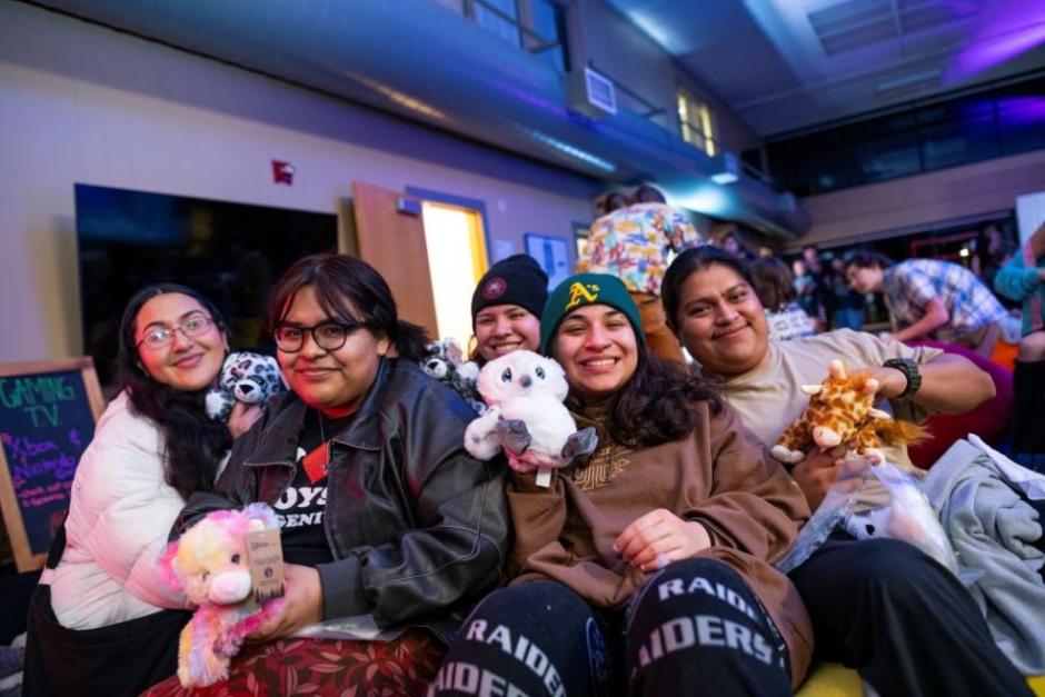 Students sitting together holding up their handmade build-a-bears and smiling 