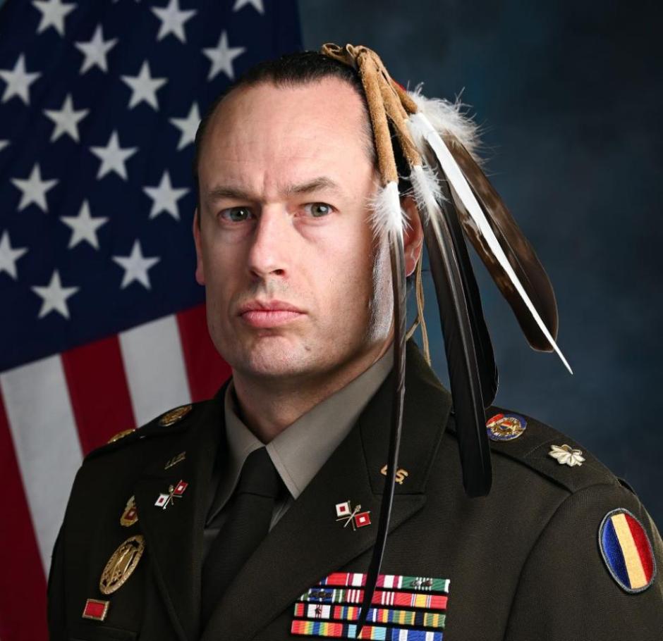 portrait of Maj. Patrick Sorensen with an American Flag behind him and eagle feathers in his hair