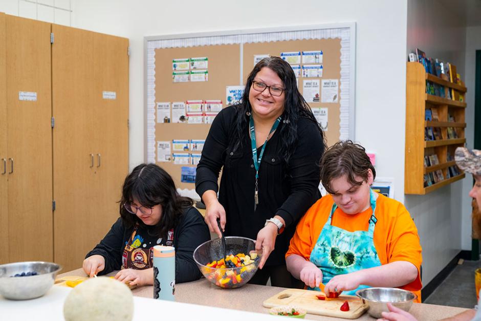 Valerie Canfield, resident teacher at Eureka High, stands between 2 students and smiles with a bowl of fruit salad in her hand. 