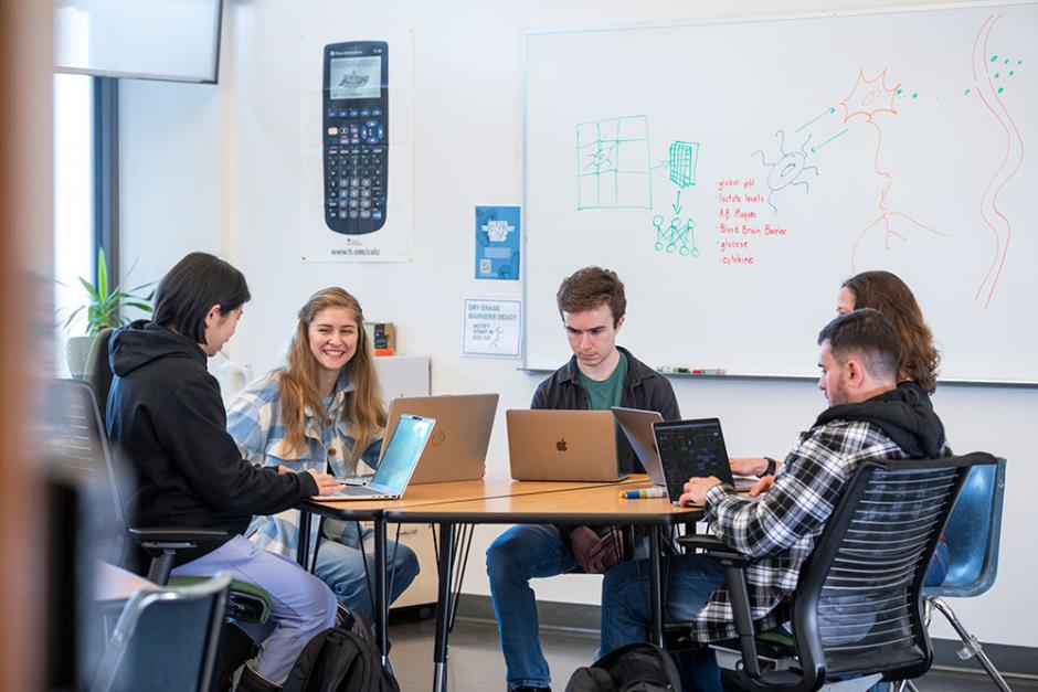 students sitting at a table on their laptops smiling and creating math models