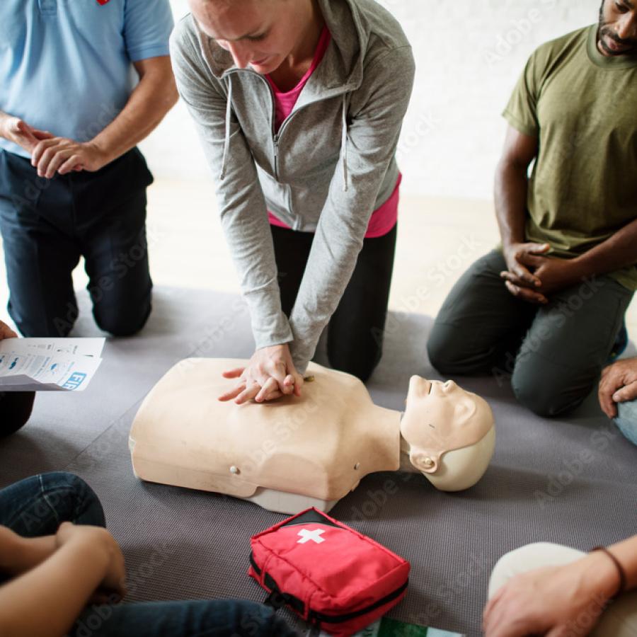 Woman performing compressions on a CPR mannakin with a group watching