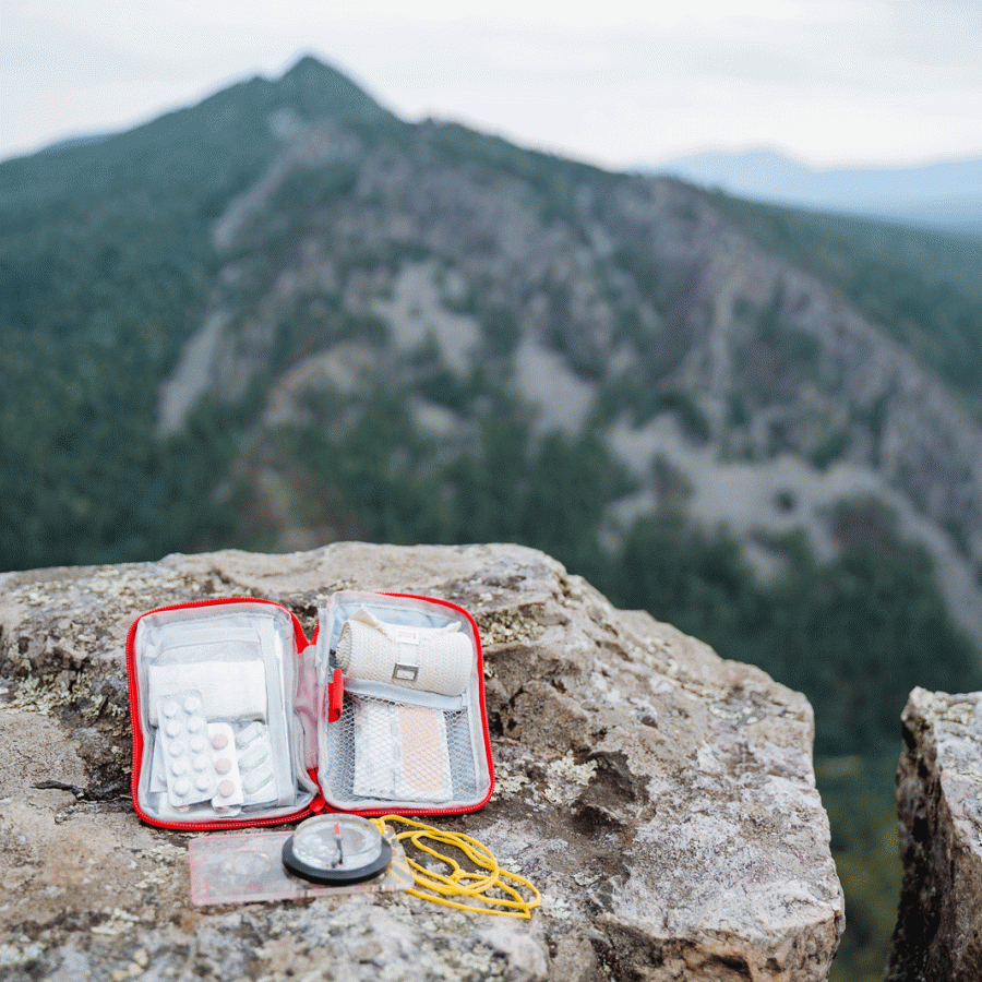 Open first aid kit and compass on a rock with mountains in the background