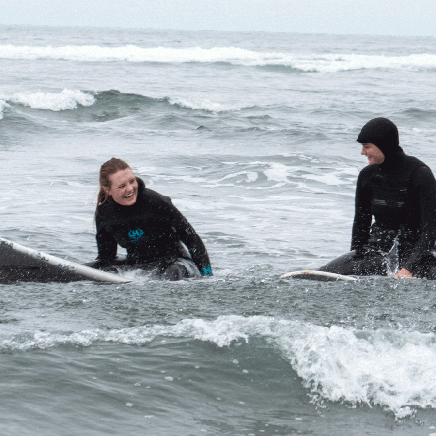 Two surfers sitting on surfboards in the ocean talking to each other