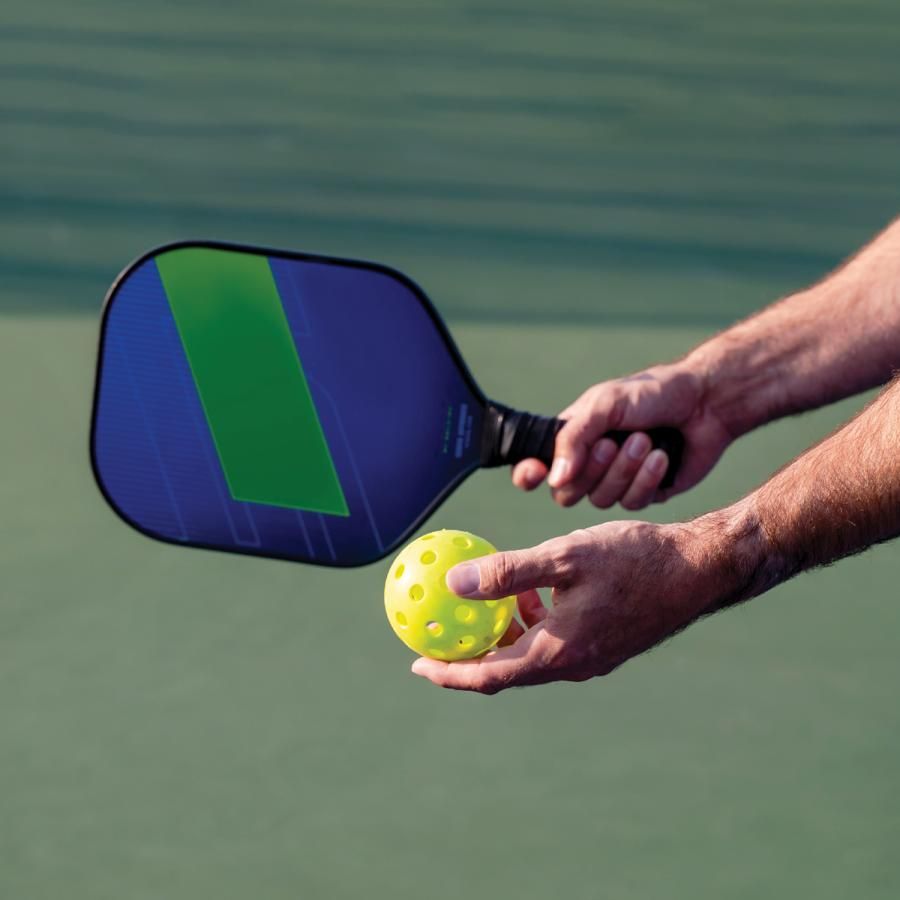 Hand holding a pickleball racket and ball Hand holding a pickleball racket and ball