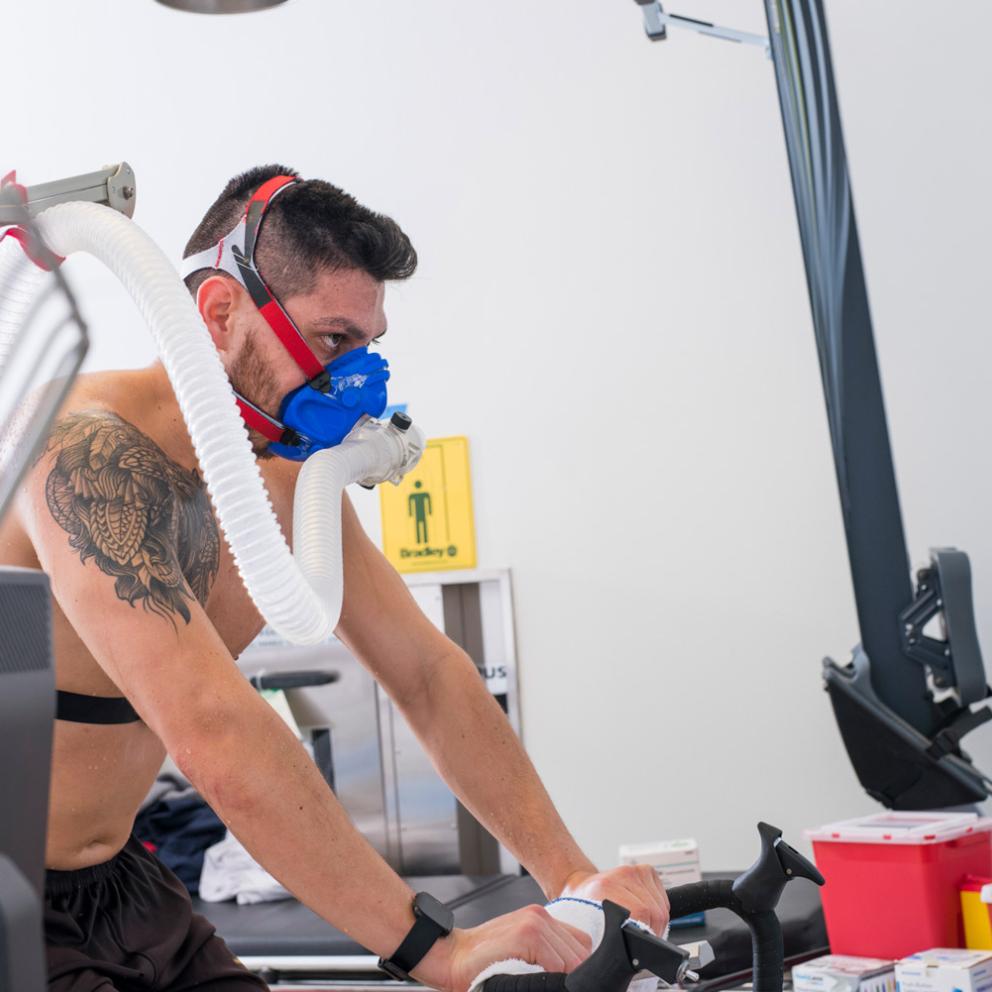 student on a bike in a lab with breathing equipment on