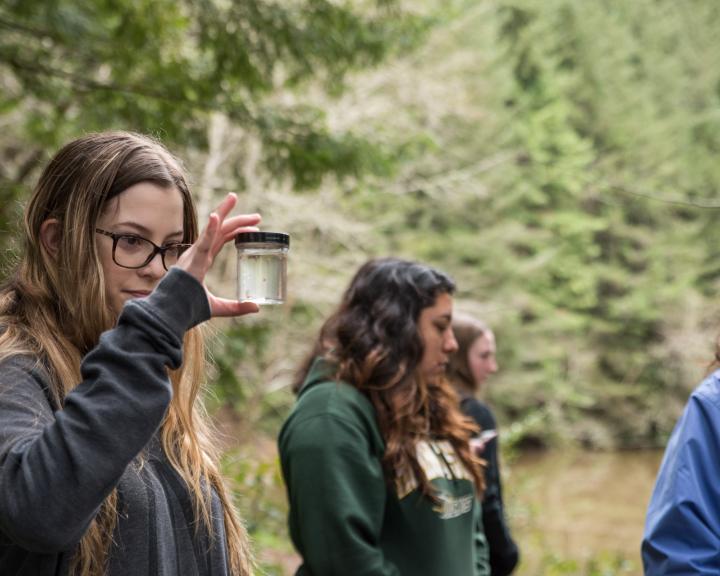 students in the field with one holding a jar up with a sample in it