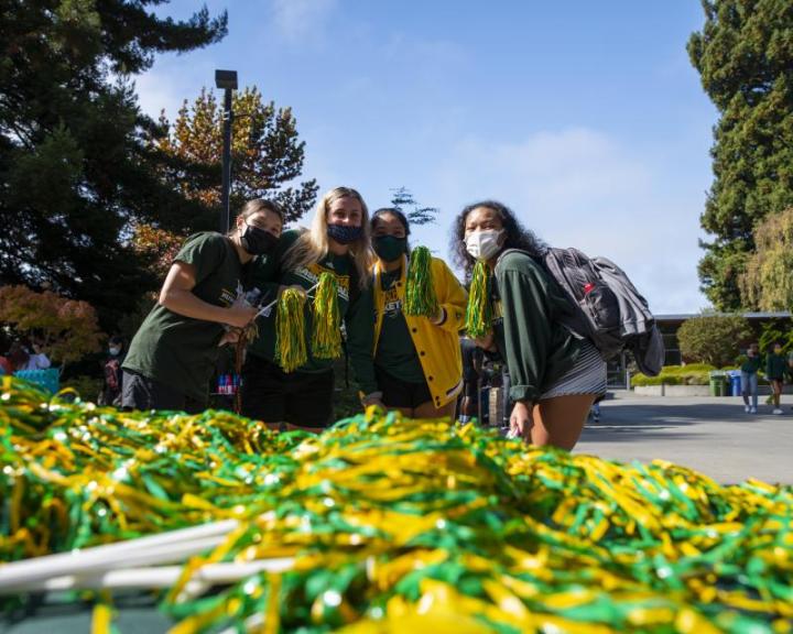 Students standing in a group smiling with green and gold pom poms in front of them