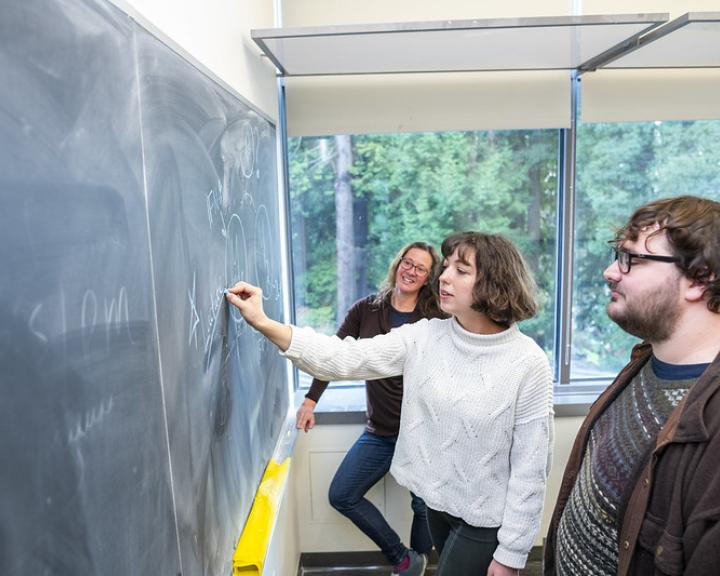 Three people standing at the chalk board