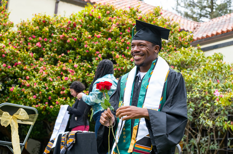 Student smiling with a rose as they cross the stage during black graduation 