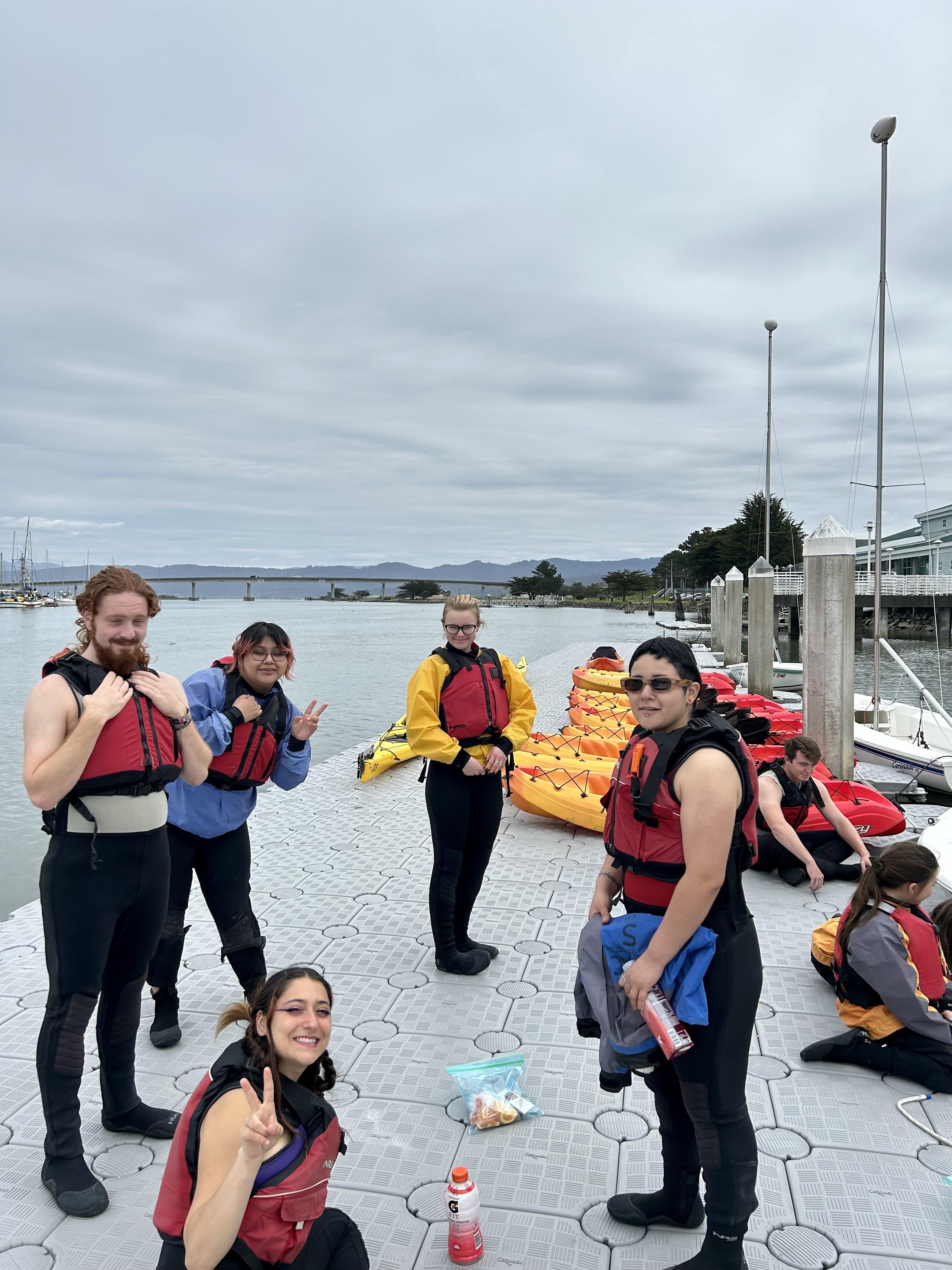 LEAP volunteers and students from Orick School sit on the dock before a kayaking trip on the Humboldt Bay Aquatic Center with Center Activities (Spring 2023)